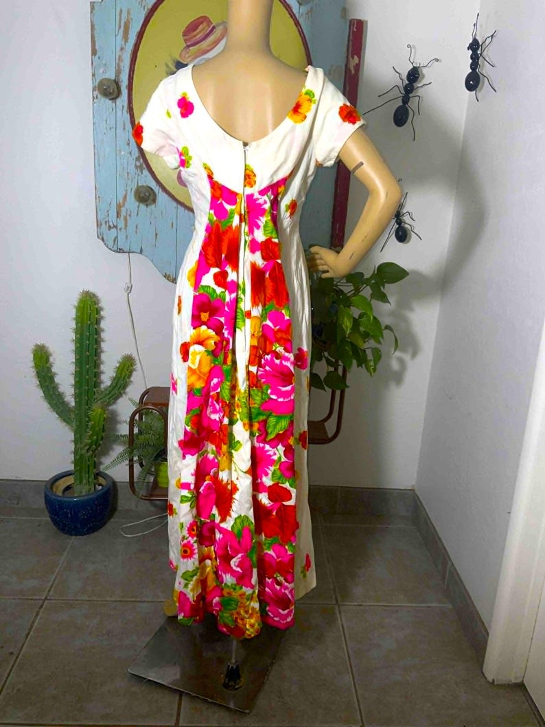 May include: A vintage white maxi dress with a scoop back and short sleeves. The dress features a vibrant floral pattern in shades of pink, red, orange, and yellow. The flowers cascade down the back of the dress, creating a bold and eye-catching design.