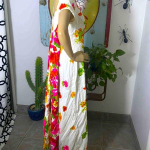 May include: White vintage maxi dress with a vibrant floral print in shades of pink, orange, and yellow. The dress features short sleeves and a flowing silhouette. The floral pattern is concentrated on the side and scattered across the front.