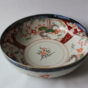 May include: A large, white ceramic bowl with a blue and red floral design. The bowl has a wide rim and a deep, round body. The floral design is intricate and features a variety of flowers, leaves, and branches.
