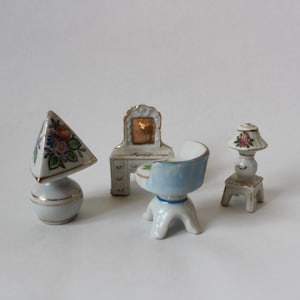 以下が含まれることがあります： 鏡台、椅子、ランプ、ランプシェードを含む、ミニチュアの磁器製の家具のセット。これらの作品は、花柄と金のアクセントで描かれています。