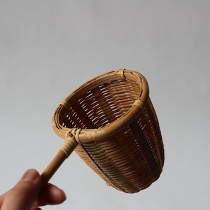 May include: A brown woven bamboo tea infuser with a long wooden handle.