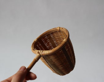 May include: A brown woven bamboo tea infuser with a long wooden handle.