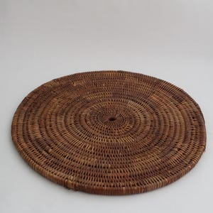 Puede incluir: Un salvamanteles redondo tejido en tonos marrones. El salvamanteles está hecho de materiales naturales y tiene un agujero central. El diseño circular presenta anillos concéntricos de fibras tejidas. Adecuado para el comedor y la decoración del hogar.