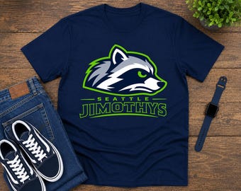 May include: A navy blue short-sleeve t-shirt featuring a graphic of a raccoon head in shades of gray, white, and lime green. Below the raccoon, the text reads SEATTLE JIMOTHYS in lime green capital letters with a lime green outline.