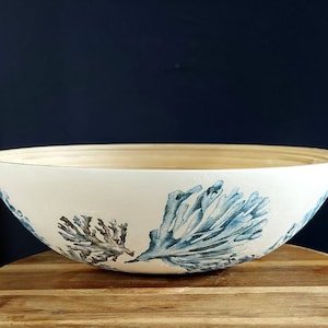 May include: A white ceramic bowl with a bamboo rim, featuring a blue and brown watercolour design of coral. The bowl is sitting on a wooden surface.