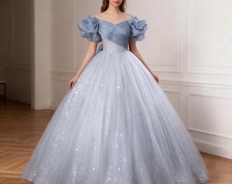 Könnte beinhalten: Hellblaues Ballkleid mit Off-Shoulder-Design und Herzausschnitt. Das Oberteil hat geraffte Details und Puffärmel. Der Rock besteht aus Tüllschichten mit funkelnden Akzenten.