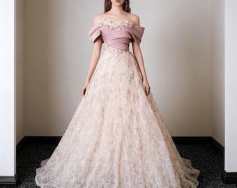Könnte beinhalten: Ein formelles Kleid mit einem blushfarbenen, schulterfreien Oberteil und einem weiten Rock. Das Oberteil hat ein mehrschichtiges Design mit floralen Verzierungen. Der Rock besteht aus einem zarten, strukturierten Stoff, der einen romantischen Look erzeugt.