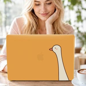 Può includere: Un adesivo per laptop color giallo senape con un'illustrazione minimalista di un'oca bianca dal collo lungo, con un piccolo becco arancione e una minuscola guancia rosa. L'oca è posizionata sul lato destro del coperchio del laptop.