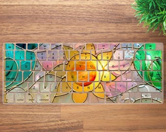 May include: A keyboard cover with a colorful floral design. The design features a large yellow and orange flower in the center, surrounded by green, blue, and pink accents. The keys are visible through the design.