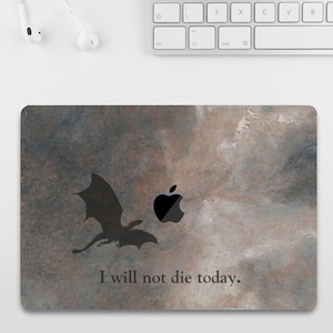 Könnte beinhalten: Laptop-Skin mit einer Drachensilhouette, einem Apple-Logo und dem Text "I will not die today." Das Design hat einen strukturierten, gesprenkelten Hintergrund in Grau- und Brauntönen.