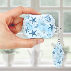 May include: A light blue AirPod case with a matching keychain, both decorated with dark blue starfish and seashell illustrations. The case has a silver metal ring for the keychain. The design is set against a light blue watercolor background.
