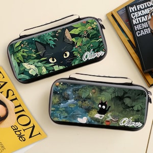 May include: Two black pencil cases with a black cat design. One case features a cat peeking through green foliage, and the other shows a cat reading by a pond. Both cases have the name "Oliver" in a script font.