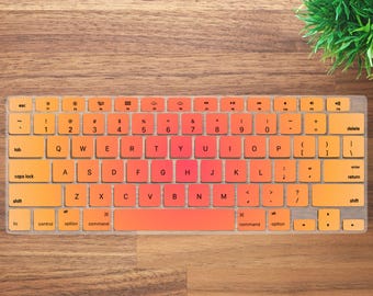 May include: A keyboard cover with an orange and red gradient design. The cover is transparent and fits over the keys, with letters and symbols visible. The keyboard cover is on a wooden surface.