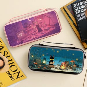 May include: Two rectangular zippered cases with illustrated designs. One is pink with a purple and pink interior scene of a cat on a desk. The other is black with a blue and green outdoor scene with a cat reading a book.