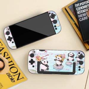 May include: Two Nintendo Switch consoles with matching decorative skins. The skins feature a pastel watercolor design with panda bears, flowers, and ducks. The consoles are black with black buttons and joysticks.
