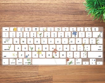 May include: A white keyboard with a floral design. The keys have a white background with black lettering. The floral design is in shades of yellow, blue, and green.