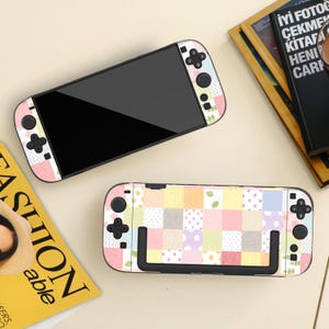 Op de afbeelding: Twee Nintendo Switch-consoles met kleurrijke skins. De skins hebben pastelkleurige vierkanten, stippen en bladeren. De consoles zijn zwart met zwarte knoppen en joysticks. Eén console is open en toont het scherm.