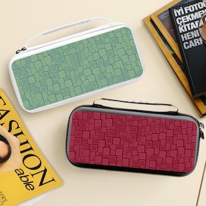 Puede incluir: Dos estuches rectangulares con asas. Uno es blanco con un patrón de cuadrados verdes y amarillos. El otro es negro con un patrón de cuadrados rojos. Ambos estuches tienen cierre de cremallera.