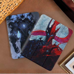 Könnte beinhalten: Zwei Tablet-Hüllen mit Fantasy-Kunst. Eine Hülle zeigt eine dunkelblaue und schwarze Figur mit einem leuchtenden Zentrum. Die andere Hülle zeigt einen rot-schwarzen Charakter mit blauäugigem Gesicht und roten Akzenten.