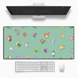 Può includere: Un tappetino per mouse rettangolare con uno sfondo verde chiaro con vari personaggi dei cartoni animati in diversi colori. Una tastiera e un mouse bianchi sono sotto e un monitor del computer è sopra.