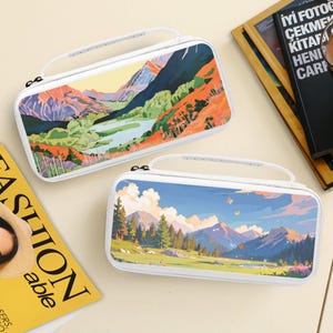 May include: Two rectangular white carrying cases with top handles, each featuring a colorful landscape print. One case displays a mountain lake scene with orange and green foliage, while the other shows a mountain range with trees and butterflies.