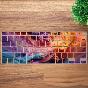 May include: A keyboard featuring an abstract design in shades of purple, orange, and blue. The keys are arranged in a standard layout, with letters, numbers, and function keys. The overall design is artistic and colourful.