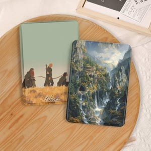 Op de afbeelding: Twee rechthoekige telefoonhoesjes. Eén heeft een landschap met figuren, de naam "Chris" staat onderaan gedrukt. De andere hoes toont een schilderachtig uitzicht op een waterval en bergen, met de naam "Oliver" onderaan gedrukt. Beide hoesjes liggen op een houten dienblad.