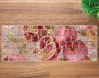 May include: A keyboard skin featuring a watercolor design of pomegranates in shades of pink, red, and gold. The keys are visible with the standard QWERTY layout. The design includes gold leaf accents and botanical elements.