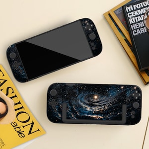 Może przedstawiać: Dwie przenośne konsole do gier z kosmicznym wzorem. Jedna konsola jest skierowana do góry, wyświetlając czarny ekran. Druga konsola jest skierowana w dół, pokazując kosmiczny wzór ze stojakiem. Konsole mają czarne przyciski i joysticki.