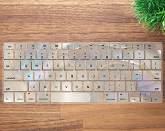 May include: A clear keyboard cover with a shimmering iridescent design. The cover is designed to fit a standard laptop keyboard and features a variety of keys, including function keys, arrow keys, and number keys.