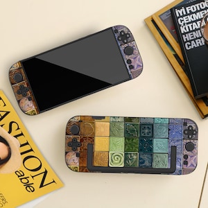 Op de afbeelding: Twee draagbare gameconsoles met decoratieve hoezen. De ene console is zwart met een patroon aan de zijkanten. De andere console heeft een zwart scherm en een kleurrijk, mozaïekachtig ontwerp op de achterkant, met vierkanten in verschillende kleuren en patronen.