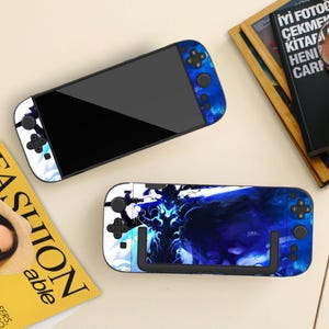 May include: Two blue and white gaming console skins with a dark blue and white abstract design. One skin is attached to a console, the other is separate. The consoles have black screens and black control buttons.