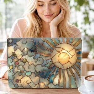 May include: A laptop skin featuring a stained glass design of a bright yellow sun with radiating beams surrounded by swirling blue and cream clouds. The artwork includes small circular accents in shades of pink, green, and gold, all outlined in dark lines.
