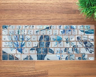 May include: A keyboard cover with a blue and white watercolor design featuring jellyfish, coral, and a whale shark. The cover is made of clear plastic and fits over a standard keyboard.