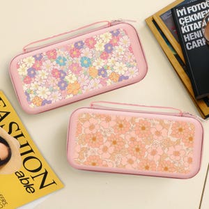 Peut inclure: Deux étuis roses à fermeture éclair avec des motifs floraux. L'un présente un assortiment coloré de fleurs, tandis que l'autre arbore un motif floral pêche. Les deux étuis ont une poignée et une fermeture éclair, idéaux pour ranger des appareils électroniques.