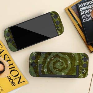 May include: A handheld video game console featuring a dark green skin with a swirling pattern and white star outlines. The device includes a black screen, directional buttons, and joysticks, with the same green star pattern on the back casing.