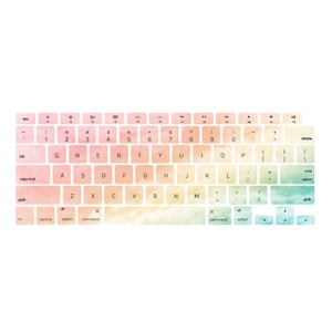 Puede incluir: Una funda para teclado de portátil con un diseño de acuarela en tonos rosa, amarillo y azul. La funda muestra todas las teclas y símbolos estándar.