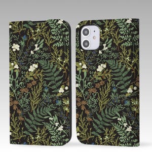 Puede incluir: Una funda de teléfono negra con un patrón floral que presenta hojas verdes, bayas blancas y piñas marrones.