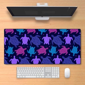 May include: A rectangular desk mat featuring a repeating pattern of stylized sea turtles in shades of blue, purple, and pink on a dark blue background. A white keyboard and mouse are visible below the mat.