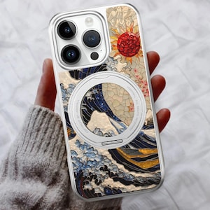 May include: Clear phone case featuring a Japanese-inspired design with a red sun, blue waves, and floral accents. The case has a silver magnetic ring and a clear border, offering protection and style.