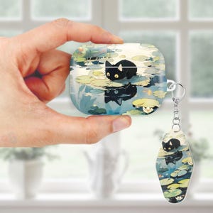 May include: A wireless earbud case and a keychain with a matching design. The case and keychain feature a black cat illustration on a pond with lily pads. The cat is reflected in the water, creating a mirrored effect.