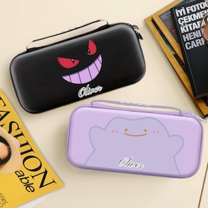 Könnte beinhalten: Zwei rechteckige Etuis mit Reißverschluss. Eines ist schwarz mit einem roten und lila Cartoon-Gesicht und dem Namen "Oliver". Das andere ist hellviolett mit einem Cartoon-Wolken-Gesicht und dem Namen "Oliver".