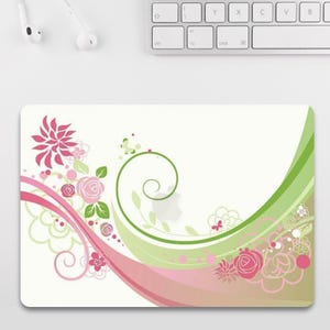 May include: A rectangular mousepad with a floral design. The design features pink and green swirls, flowers, and leaves on a white background. A pink flower is on the left side, and a green swirl is on the right side.