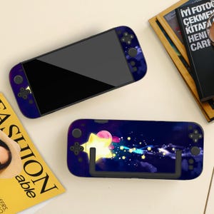 Könnte beinhalten: Zwei Nintendo Switch-Konsolen mit individuellen Skins. Eine Konsole hat ein dunkelblaues und violettes Farbverlauf-Design. Die andere hat eine farbenfrohe Grafik eines Sterns und eines rosa Charakters vor einem Sternenhintergrund.