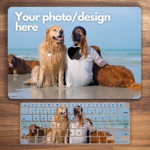May include: A laptop skin with a design featuring two golden retrievers and a person sitting on a beach. The skin has a blue background and the text "Your photo/design here" at the top. The keyboard has a design featuring a collage of images of dogs.
