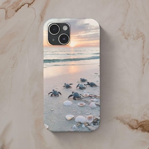 May include: A phone case with a sunset beach scene featuring baby sea turtles walking on the sand. The case has a camera cutout and a white background.