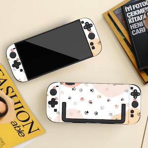 May include: Two white Nintendo Switch consoles with a paw print design. The consoles have black screens and black buttons. One console is fully assembled, and the other is disassembled. The paw prints are in shades of brown, gray, and black.