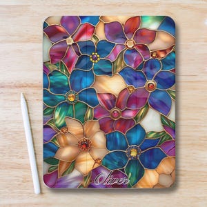 Puede incluir: Una funda rectangular para tableta con un diseño floral de vidriera en tonos azules, morados, rojos y dorados. Las flores tienen centros con forma de joya y están delineadas en dorado. El nombre "Oliver" está escrito en cursiva en la parte inferior.
