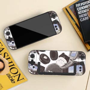 Op de afbeelding: Twee Nintendo Switch-consoles met decoratieve skins. De ene console heeft een camouflagepatroon, terwijl de andere een zwart-wit illustratie toont van een stripfiguur met een telefoon en pootafdrukken. De consoles liggen op een lichte ondergrond.