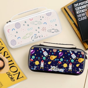 May include: Two hard-shell cases with space-themed designs. One is white with rockets, planets, and stars, and the name "Oliver". The other is navy blue with rockets, planets, stars, and the name "Oliver". Both have a handle and zip.